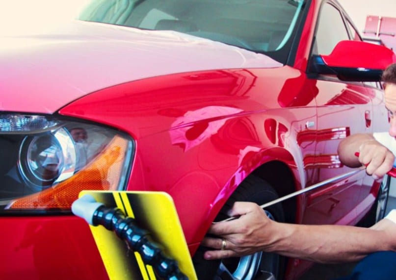 Technician repairing a dent in a red vehicle’s front fender