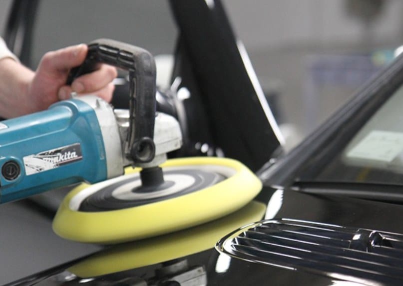 Powered polisher buffing a dark vehicle’s paintwork