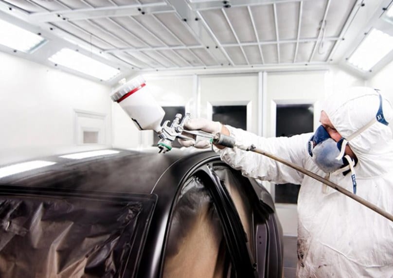 Painter spraying a masked vehicle inside a paint booth