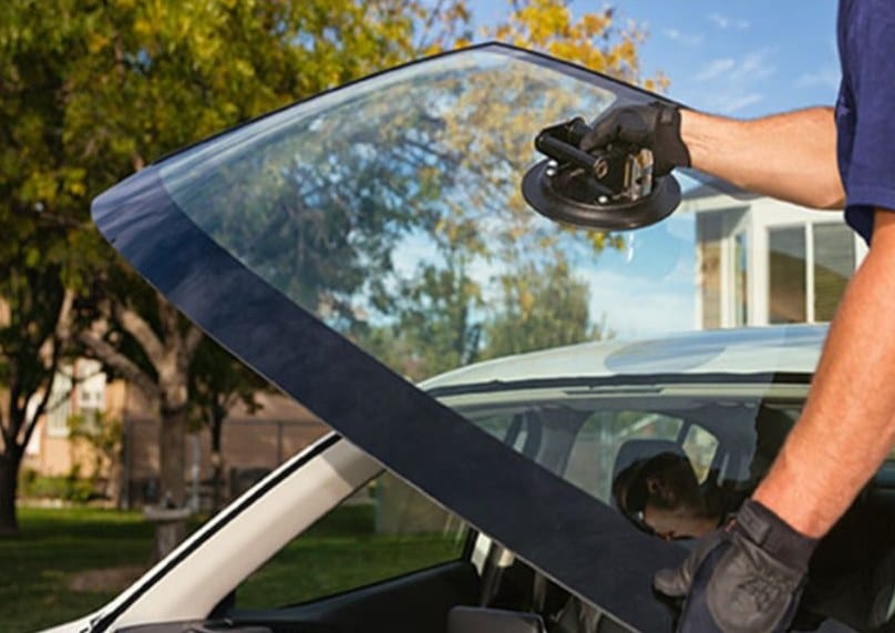 Technician lifting windshield glass with a suction-cup tool